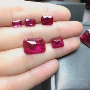 May include: Five red ruby gemstones of varying sizes, displayed on a hand. The gemstones are cut in a rectangular shape with facets.