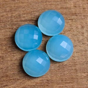 May include: Four light blue gemstone cabochons with a faceted finish. The cabochons are round and have a smooth, polished surface.