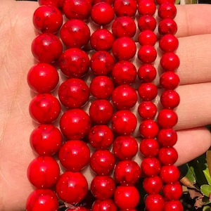 Könnte beinhalten: Eine Strähne roter Edelsteinperlen. Die Perlen sind rund und haben eine glatte, polierte Oberfläche. Sie sind auf einer durchsichtigen Gummikordel aufgefädelt.