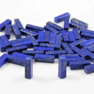 May include: A collection of small, rectangular lapis lazuli gemstone beads. The beads are a deep blue color with flecks of gold pyrite.