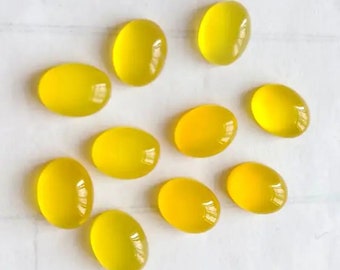 May include: Ten oval-shaped yellow gemstones, likely citrine, arranged on a white surface.