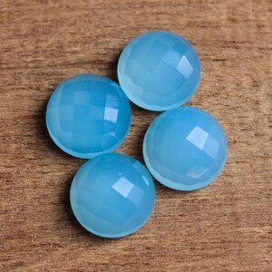 May include: Four light blue gemstone cabochons with faceted surfaces. The cabochons are round and have a smooth, polished finish.