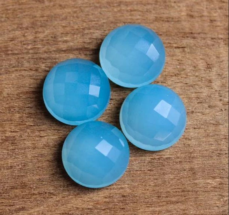May include: Four light blue gemstone cabochons with faceted surfaces. The cabochons are round and have a smooth, polished finish.
