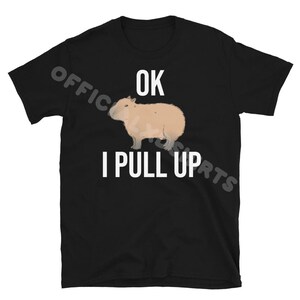 May include: Black t-shirt featuring a light brown capybara illustration with the text "OK I PULL UP" in white. The shirt is made of a soft material and is suitable for casual wear.