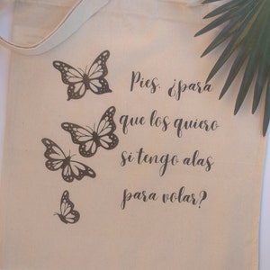 May include: A beige canvas tote bag with brown butterfly graphics and the text "Pies. ¿para que los quiero si tengo alas para volar?"