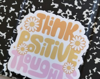 May include: A pink, yellow, and orange sticker with the text "Think Positive Thoughts" in a retro font. The sticker is decorated with white daisies.