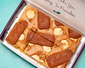 May include: A box of individually cut squares of a dessert made with Lotus Biscoff cookies, white chocolate, and caramel. The box is open and the dessert is visible. The box has the text "Take You Away To Paradise" on the lid.