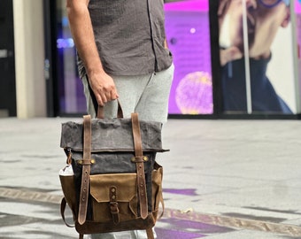 May include: A brown and black canvas backpack with leather straps and buckles. The backpack has a large main compartment and a smaller front pocket.