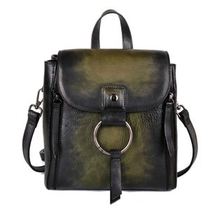 Handcrafted Green leather backpack for women, featuring a classic design with a large metal ring, front strap closure, and side zipper details, showcased in an artistic setting with purple accents