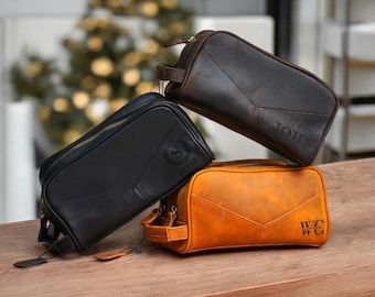 May include: Three leather wash bags with personalised names. The bags are stacked on top of each other. The top bag is brown, the middle bag is black, and the bottom bag is tan.