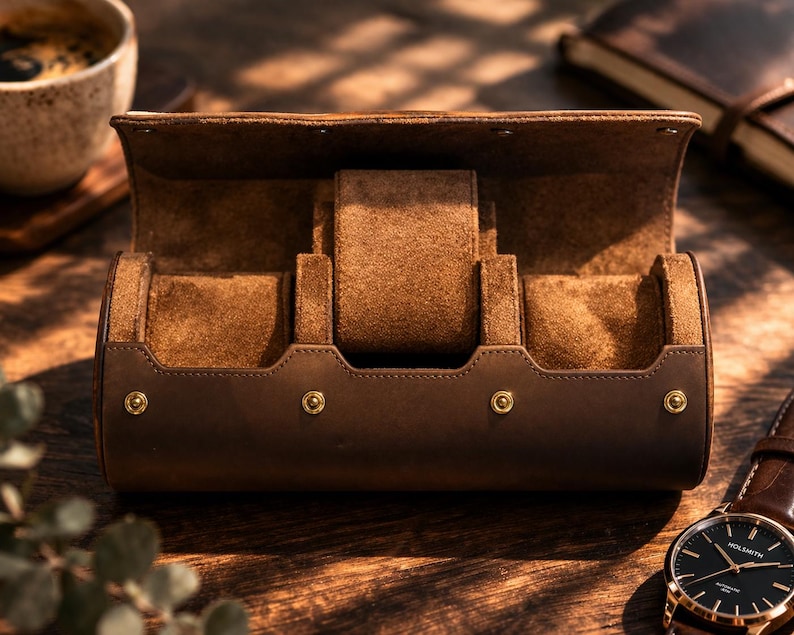 May include: A brown leather watch case with a suede interior, open to display three watch compartments. The case has gold-colored rivets and a matching brown leather strap watch is visible. The case is on a wooden surface.
