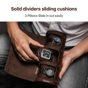 May include: A brown leather watch roll with three compartments, each holding a wristwatch. The roll is open, revealing the watches. Text at the top reads "Solid dividers sliding cushions" and "3 Pillows Slide in out easily". The roll measures 75mm wide and 55mm high.