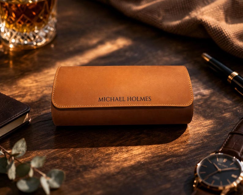 May include: A brown leather watch case with the name "MICHAEL HOLMES" embossed on the front. The case is rectangular with rounded edges and a stitched border. A wristwatch with a black face and gold accents is visible.