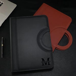 May include: Two leather binders, one black and one brown, with a ring handle and a monogrammed "M" on the front.