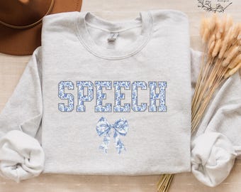 May include: A gray sweatshirt with the word "SPEECH" printed in blue and white floral letters. A blue and white floral bow is below the word.