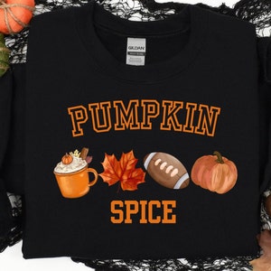May include: Black sweatshirt with the words "PUMPKIN SPICE" in orange collegiate lettering. The design includes a watercolor-style pumpkin spice latte, a fall leaf, a football, and a pumpkin.