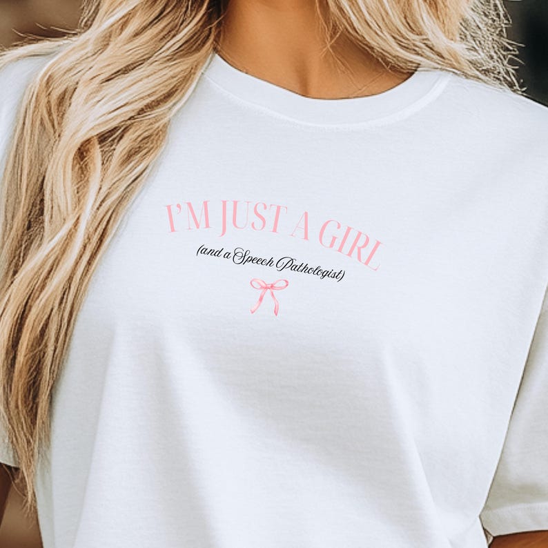 Pu&ograve; includere: Maglietta bianca con il testo "I'm just a girl (and a Speech Pathologist)" in nero con un fiocco rosa.