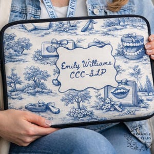 May include: A blue and white laptop sleeve featuring a toile pattern with trees, bows, and speech therapy-related graphics. The sleeve has a black border and includes the name "Emily Williams CCC-SLP" in a white, decorative frame.