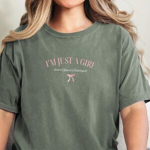 Pu&ograve; includere: Una maglietta verde con il testo "I'm just a girl (and a Speech Pathologist)" in lettere rosa con un fiocco rosa sotto.