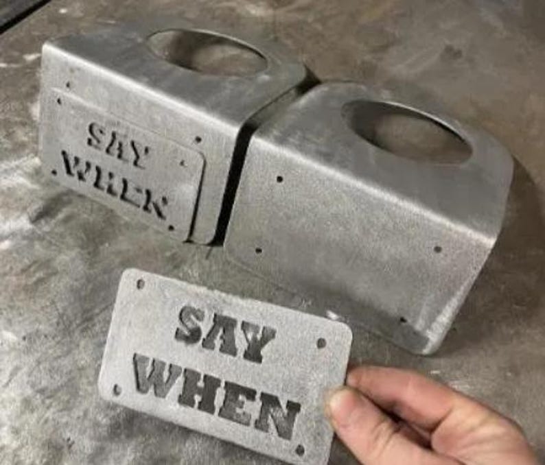 May include: Two silver-colored metal brackets with circular cutouts and a rectangular metal plate, all featuring the embossed text SAY WHEN. The components have a raw, industrial finish with visible screw holes on the plate and bracket faces.