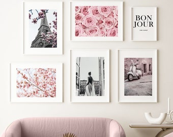 May include: A living room interior with a pink sofa and armchair, a gold coffee table, and a white wall with six framed prints. The prints feature a variety of images, including a Parisian cityscape, a floral pattern, a woman in a dress, and a vintage scooter.