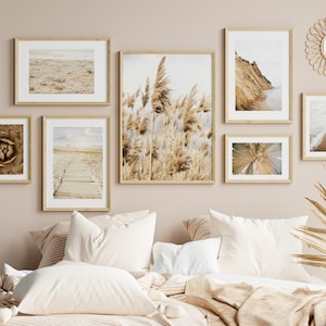 May include: A bedroom interior with a light brown wall and a bed with white bedding and a brown throw blanket. The wall is decorated with a gallery wall of framed prints featuring beach scenes, plants, and abstract designs. A woven wicker sunburst mirror hangs above the bed.