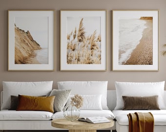 Peut inclure: Trois impressions encadrées de scènes de nature sont accrochées à un mur beige au-dessus d'un canapé sectionnel blanc. Les impressions représentent une plage de sable avec des vagues, une falaise avec une plage de sable et un champ d'herbe haute.