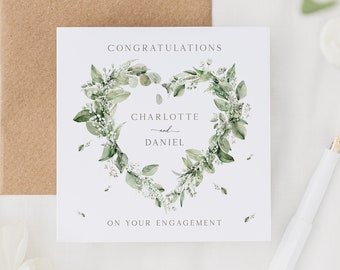 May include: Square engagement card with a heart-shaped floral wreath design. The card reads "Congratulations Charlotte and Daniel on your engagement." A kraft paper envelope and white pen are also visible.