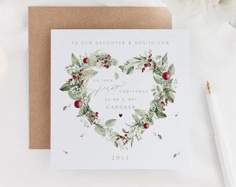 May include: A white Christmas card with a green and red heart wreath design. The card reads "To our daughter & son-in-law, On your first Christmas as Mr & Mrs Gardner, 2023".