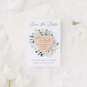 May include: A wedding announcement card with the text "Save the Date" in elegant script. The card features a wooden heart with the names "Charlotte & Daniel" and the date "12.08.27", surrounded by a floral wreath. An envelope and flowers are in the background.