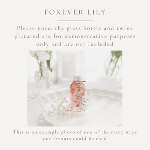May include: A small glass bottle filled with a pink liquid, sitting on a white plate with a white flower sprig. The bottle has a white tag attached with the text "A piece of our special day Charlotte & Wil 20.07.24".