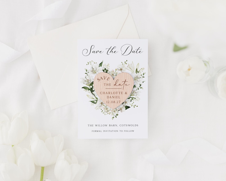 May include: A wedding announcement card with a wooden heart and floral design. The card reads "Save the Date" with the names "Charlotte & Daniel" and the date "12.08.27". Includes an envelope and white flowers.