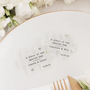 May include: Two clear acrylic puzzle pieces with the text "A piece of our special day" and the names of the couples, "Amelia & Oliver" and "Charlotte & Will", along with their wedding dates.