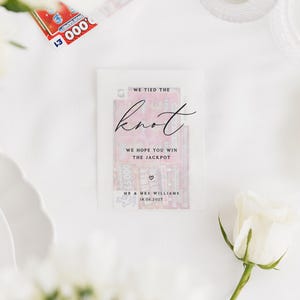 Puede incluir: Un recuerdo de boda con un billete de loter&iacute;a dentro de un sobre transl&uacute;cido. El sobre dice "WE TIED THE knot" y "WE HOPE YOU WIN THE JACKPOT". La fecha "18.06.2027" y los nombres "MR & MRS WILLIAMS" tambi&eacute;n est&aacute;n impresos.