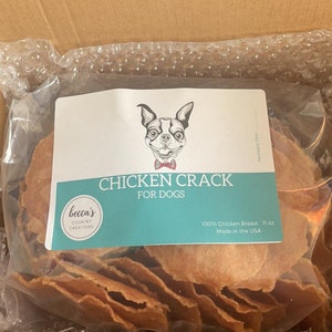 Puede incluir: Una bolsa de pl&aacute;stico transparente llena de golosinas de pollo deshidratado para perros, etiquetada como "Chicken Crack For Dogs". La etiqueta presenta un perro de dibujos animados con pajarita y el texto "100% Chicken Breast 11 oz Made in the USA."