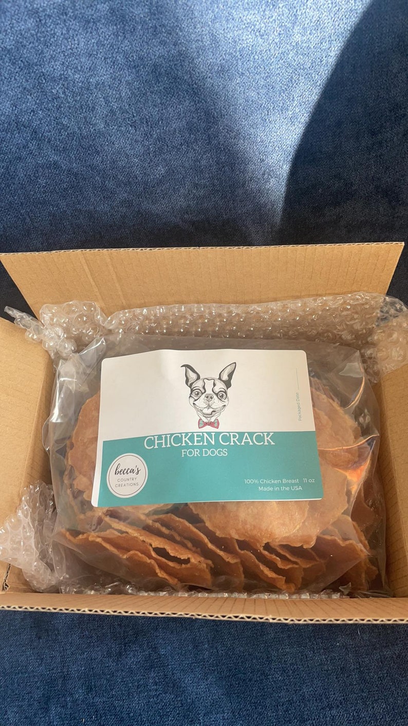 Puede incluir: Un paquete de golosinas para perros etiquetado como "Chicken Crack for Dogs" con una ilustraci&oacute;n de perro de dibujos animados. Las golosinas est&aacute;n hechas de 100% pechuga de pollo y pesan 312 gramos. El paquete est&aacute; dentro de una caja de cart&oacute;n.