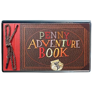 May include: A rectangular album with a brown faux leather cover featuring the text PENNY ADVENTURE BOOK in multicolored letters. The left side is red with a brown braided cord laced through metal eyelets. A small circular map graphic is below.