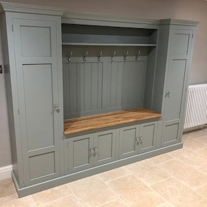 May include: A grey painted built-in storage unit with a wooden top and a bench seat. The unit has two doors on each side and a centre section with open shelves and hooks.