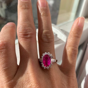 Könnte beinhalten: Ein Ring mit einem großen ovalen rosafarbenen Edelstein, umgeben von einem Heiligenschein aus kleineren Diamanten. Der Ring ist in Weißgold gefasst.