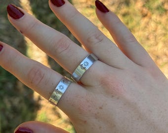 May include: Two silver rings with a sun and moon design. The rings are worn on a hand with red nail polish.