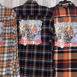 May include: Three plaid flannel shirts with a graphic print on the back. The graphic features a collage of images of Taylor Swift with the text "Taylor Swift The Eras Tour". The shirts are in brown, black, and orange plaid.