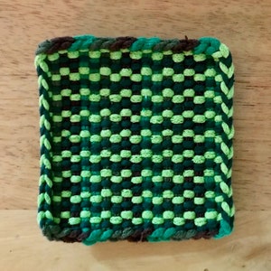 May include: A square green and brown woven coaster with a braided border.