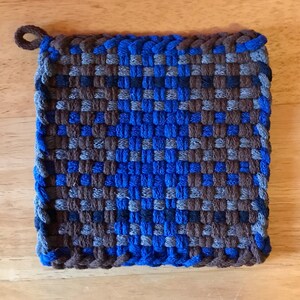 Puede incluir: Un agarrador de olla tejido azul y marrón con un lazo para colgar.
