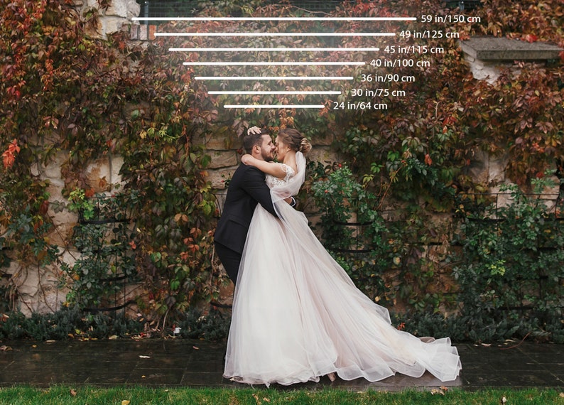 May include: A newly married couple embraces in front of a stone wall covered in autumn foliage. The bride wears a white wedding gown with a long train. The groom is in a black suit. Measurements are indicated in inches and centimeters.