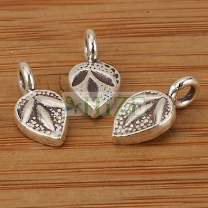 May include: Three silver leaf-shaped charms with a textured surface and a detailed design. The charms have a loop at the top for attaching to jewelry or other crafts.