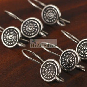 May include: Close-up of several silver-toned earrings. Each earring features a circular design with a spiral pattern. The earrings have a hook-style closure. The text "HiZE Silver" is visible in the image.