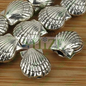 May include: A group of silver-colored metal seashell charms. The charms are detailed with ridges and lines to resemble a real seashell.