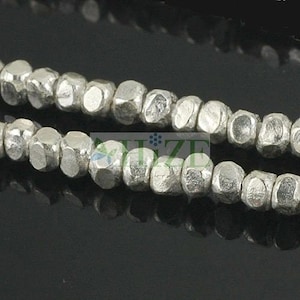 May include: Close-up of two strands of silver-colored, faceted beads. The beads have an irregular, textured surface and a metallic sheen. The beads are strung together, creating a necklace or bracelet.