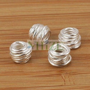 May include: Four silver-toned metal bead spacers with a twisted wire design. The spacers are round and have a hole in the center.