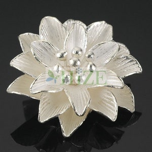May include: A silver-colored flower-shaped embellishment with a layered design. The flower has a white, pearlescent finish and is adorned with small, round, silver beads in the center.